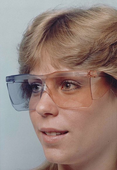 Foto van een dunne, witte vrouw met blonde haren die de Vision-Dieter glasses draagt. Het lijkt op een zonnebril met lichte glazen, eentje blauw en eentje bruin.